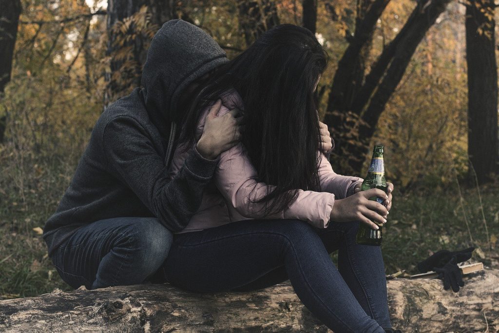 Person mit Bierflasche wird von anderer Person tröstend umarmt