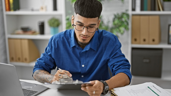 Ein junger Mann sitzt vor seinem Laptop und macht sich Notizen