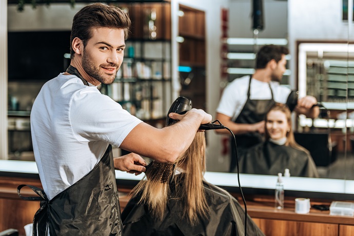 Junger Friseur fönt einer Kundin die Haare