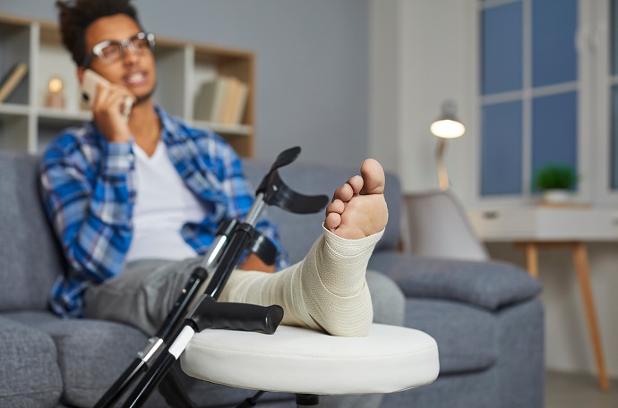 Ein Mann sitzt auf dem Sofa und hat seinen bandagierten Fuß auf einen Hocker liegen