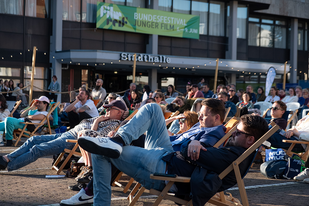 Menschen lümmeln in Liegestühlen bei einem Open-Air-Filmfestival und schauen auf eine Leinwand.
