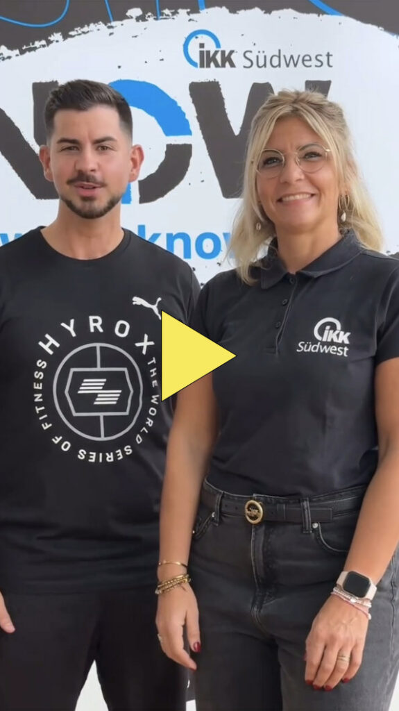 Zwei Personen stehen nebeneinander und lächeln in die Kamera. Der Mann trägt ein schwarzes Hemd mit weißem Muster, die Frau eine Brille und ein schwarzes Poloshirt mit IKK Südwest-Logo. In der Mitte ist ein gelber Play-Button eingeblendet.